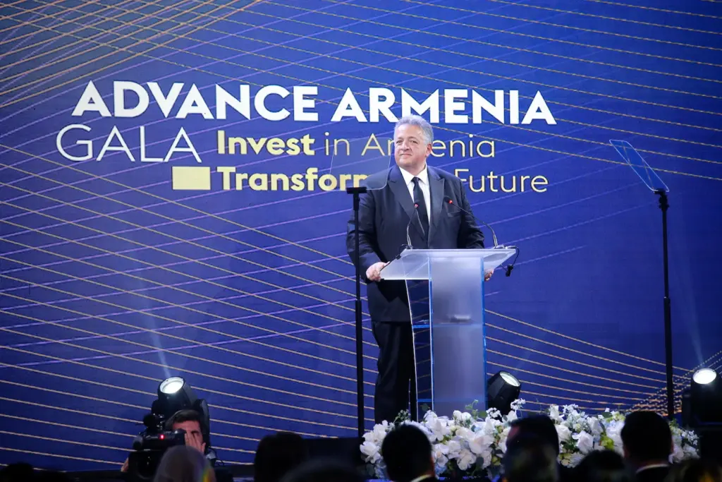 Speaker addressing guests from a podium in front of the Advance Armenia Gala screen