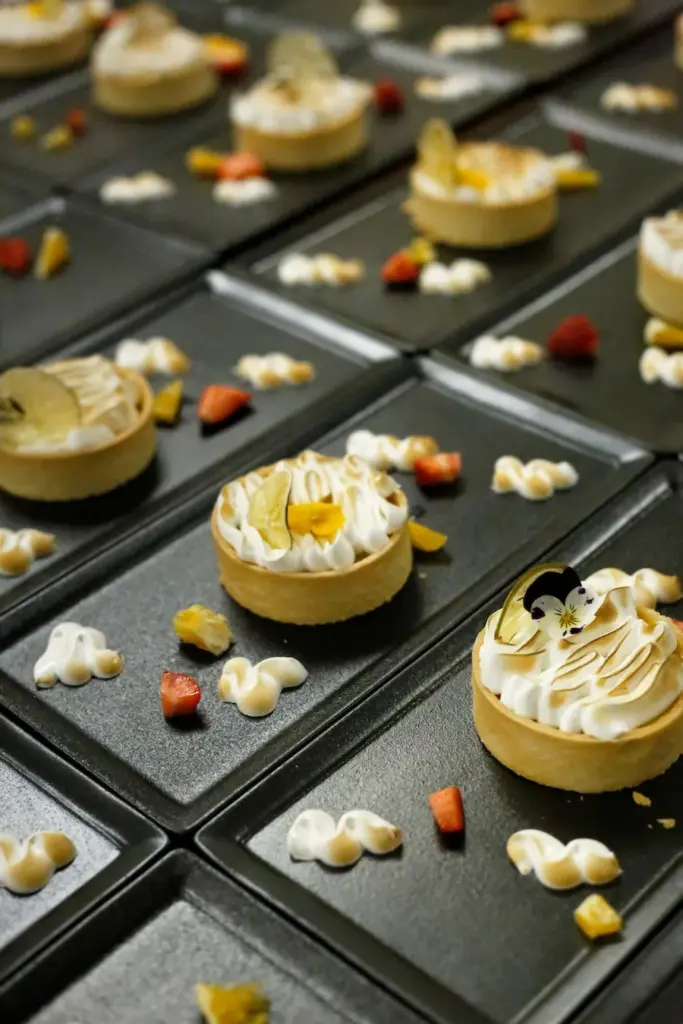 Rows of lemon meringue tartlets arranged on dark dessert plates