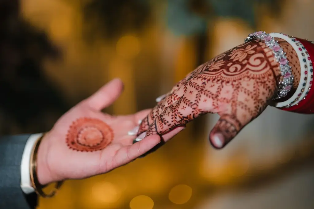 Close-up of a bride and groom's hands, one painted with intricate henna and bangles