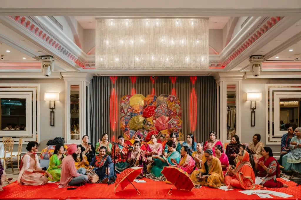 Musicians and guests in colorful traditional attire performing on a red carpet with parasols