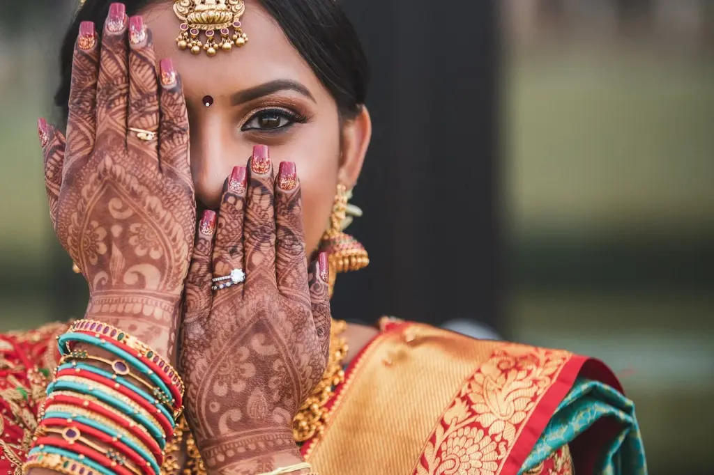 Close-up portrait of a bride with henna-painted hands and gold bridal jewelry