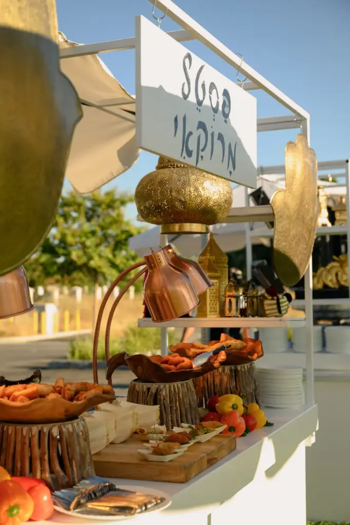 Moroccan-style food station with a brass lantern and Hebrew sign over appetizer trays