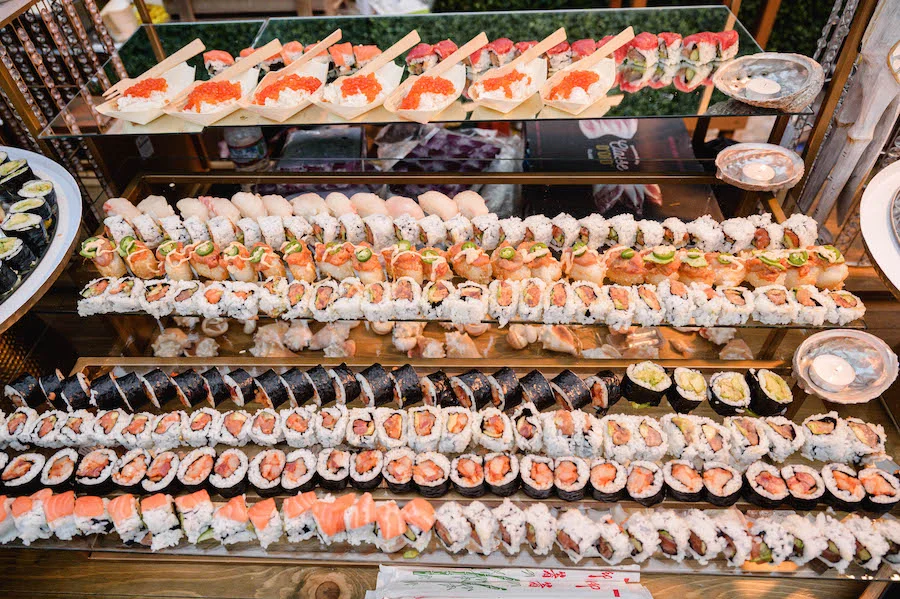 Sushi and sashimi rolls displayed in tiered rows at a catering station