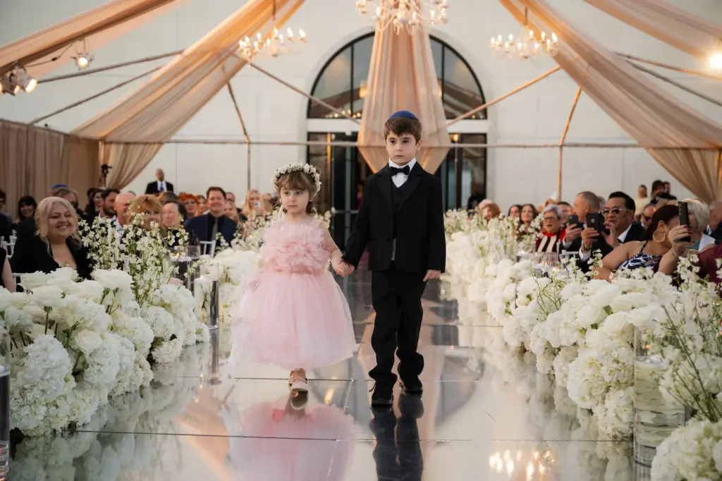 Flower girl and ring bearer walking down an aisle lined with white hydrangeas