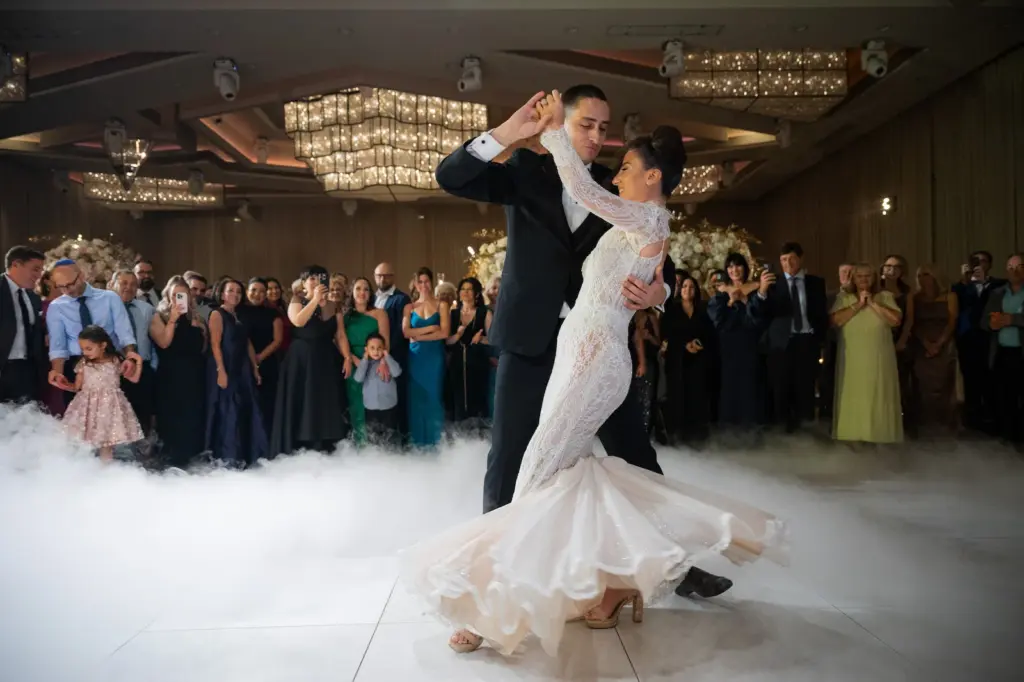 Bride and groom's first dance on the dance floor amid dry ice fog as guests watch