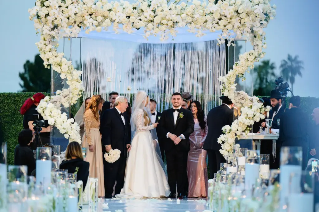 Wedding party processing under a floral canopy as the bride walks with her father