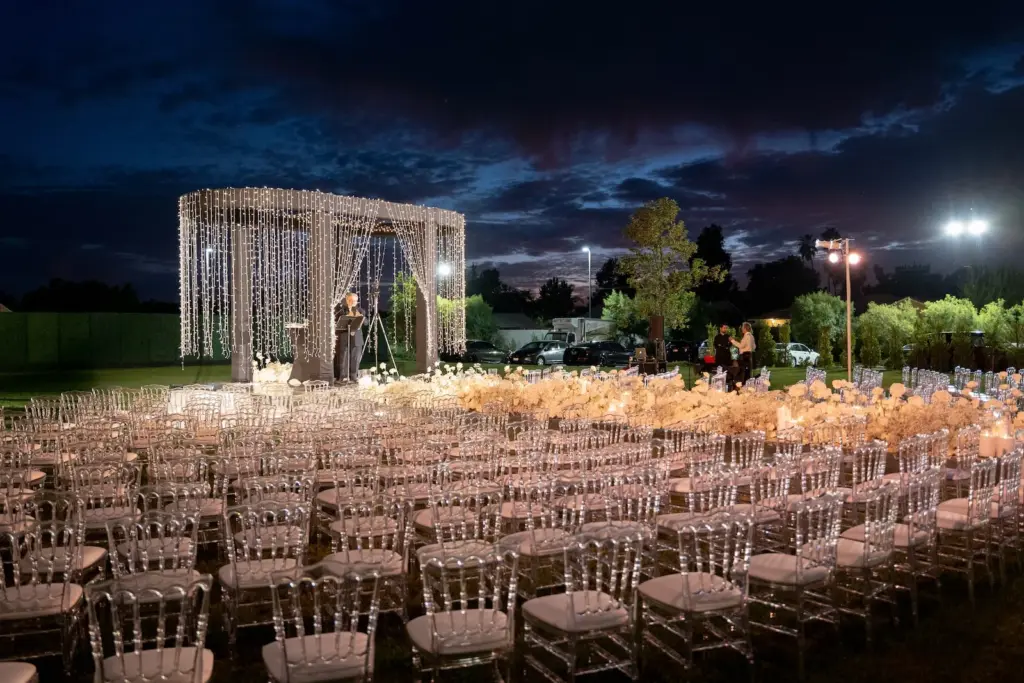 Wide night view of an outdoor ceremony with a string-light chuppah and empty chairs