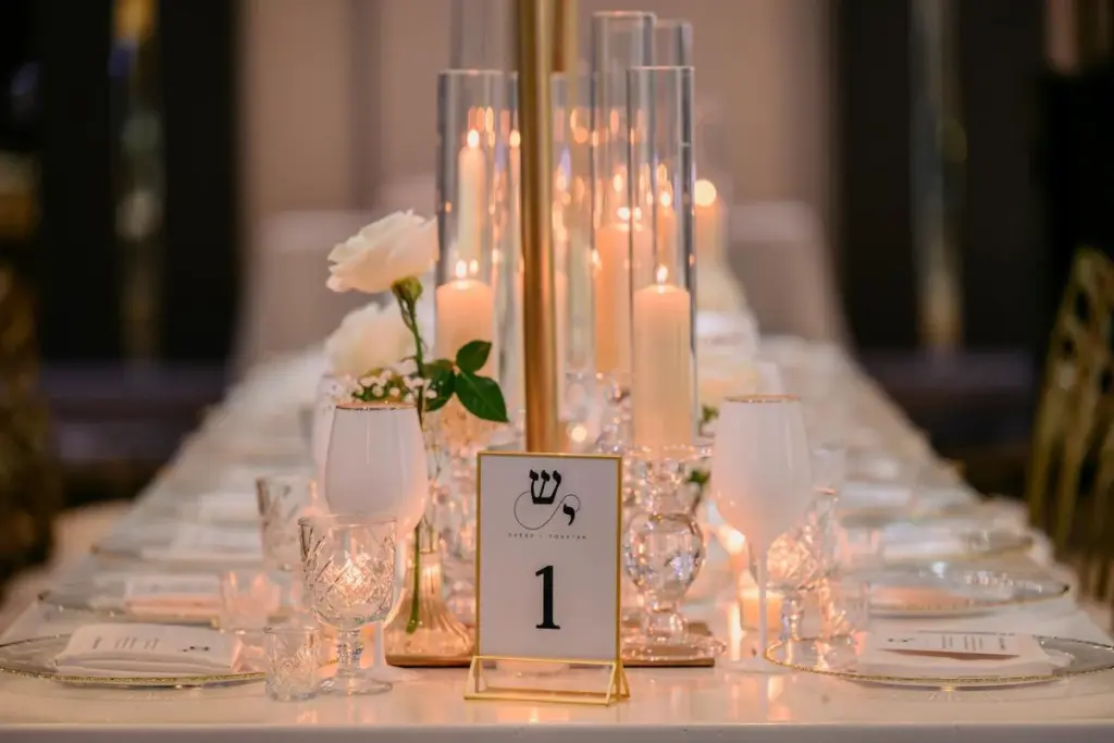 Elegant table setting with a gold-rimmed charger, place card, candles and white roses