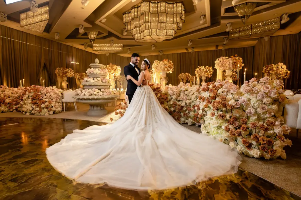 Reception stage backdrop with cascading floral arches and a stone fountain by candlelight
