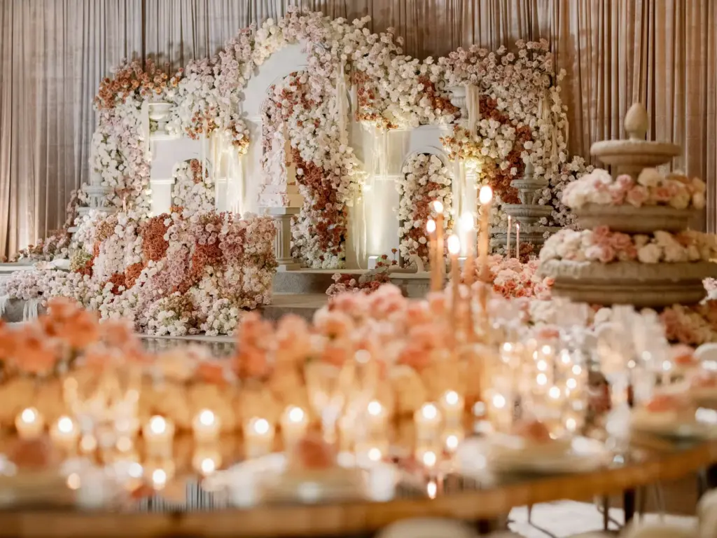 Reception hall with a floral arch stage, candelabra and round tables set with blush florals