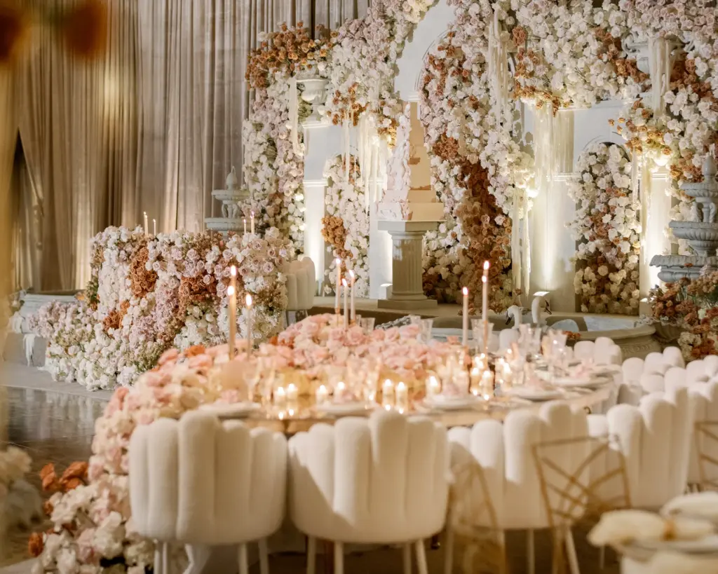 Curved banquet table with tall candles, blush centerpieces and cream scalloped chairs
