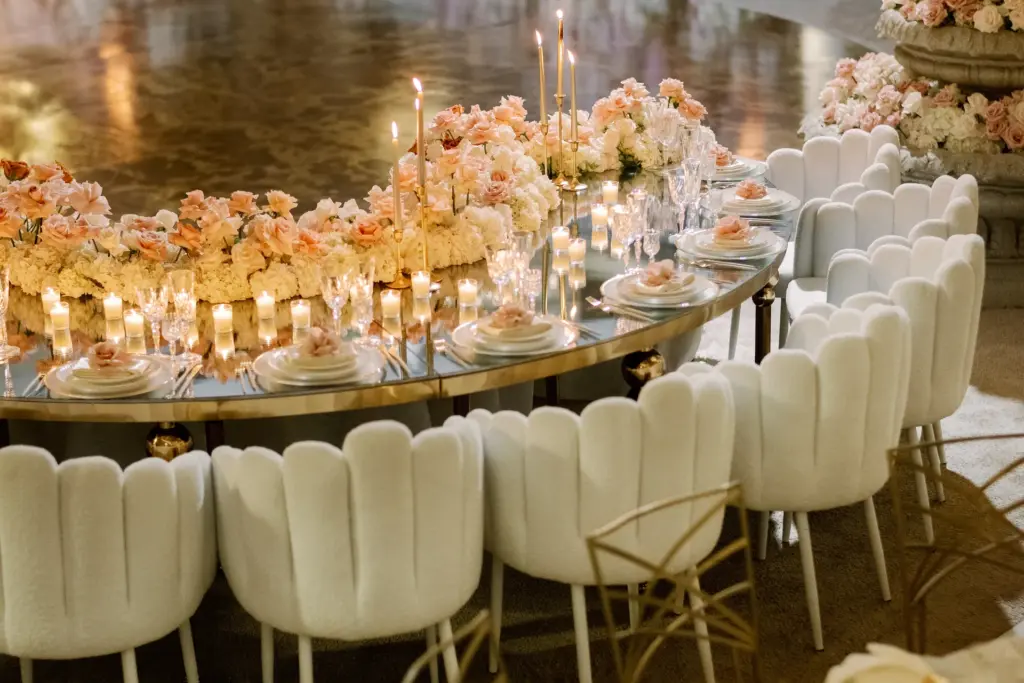 Curved head table with candles, pink floral centerpieces and gold accent chairs