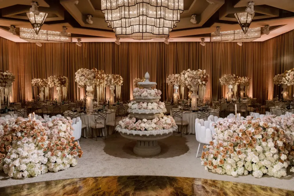 Grand ballroom reception with a tiered floral fountain centerpiece and floral wall backdrop