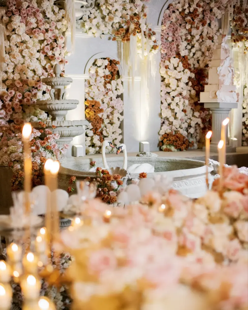 Tiered stone fountain with a pair of swans amid a candlelit floral display