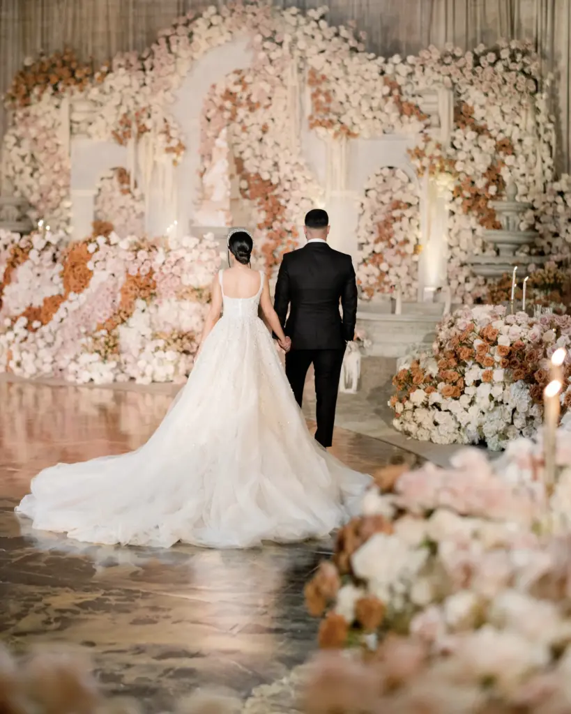 Bride and groom walking hand in hand toward a floral wedding backdrop