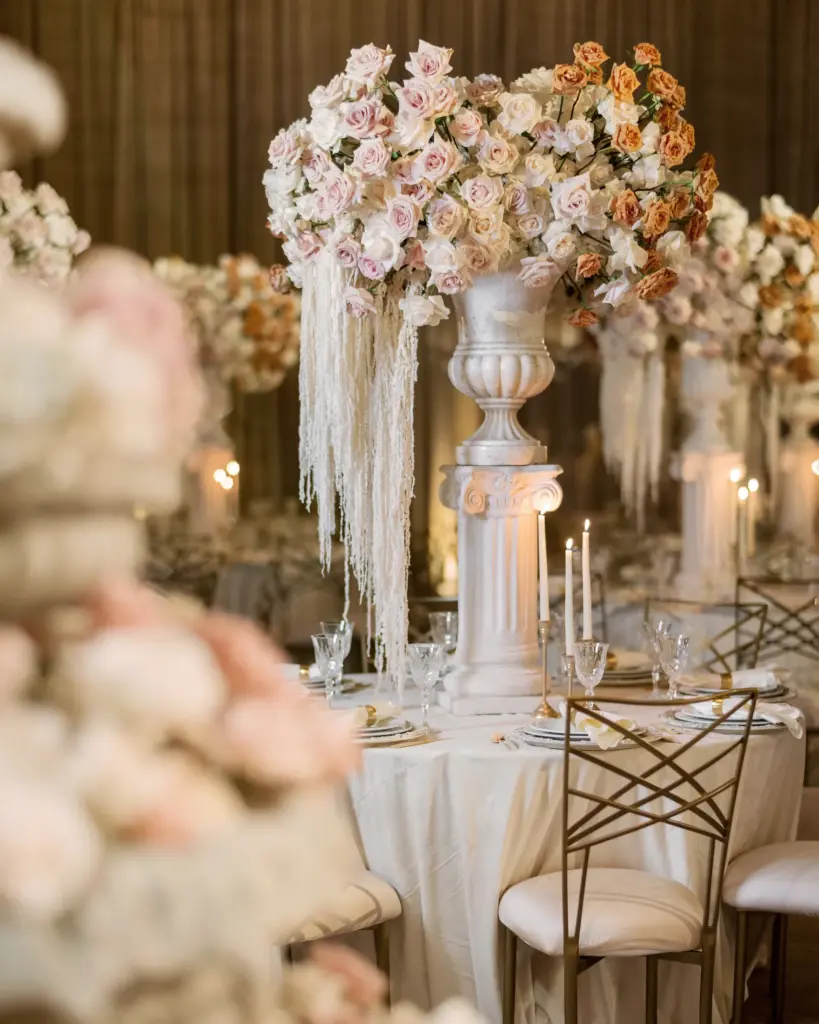 Tall floral centerpiece in a white urn with trailing ribbons on a pedestal