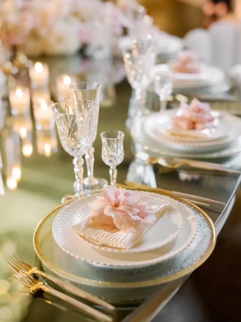 Close-up place setting with a gold-rimmed charger, pink rose and crystal stemware