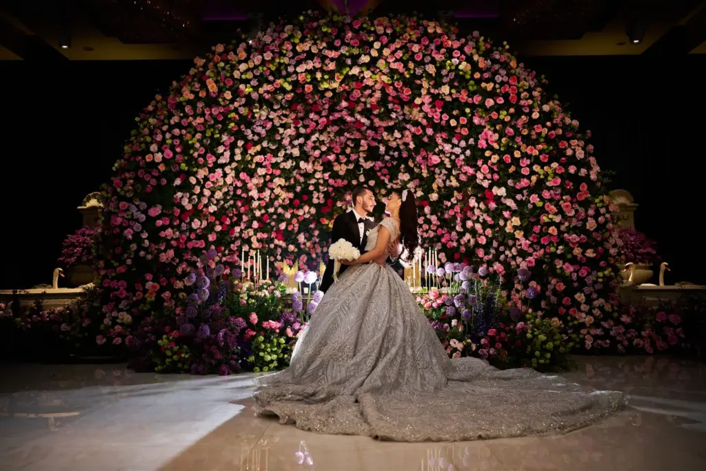 Bride and groom embracing in front of a large pink and white floral backdrop
