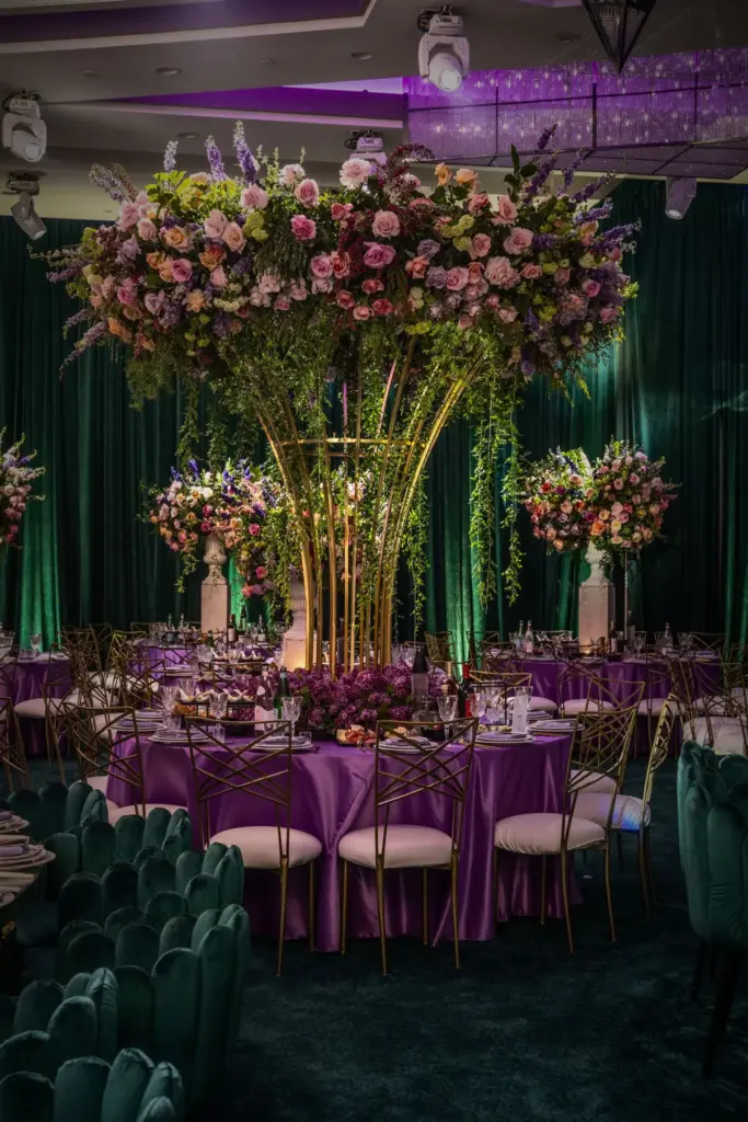 Round banquet table with purple linens set beneath a tall gold floral centerpiece