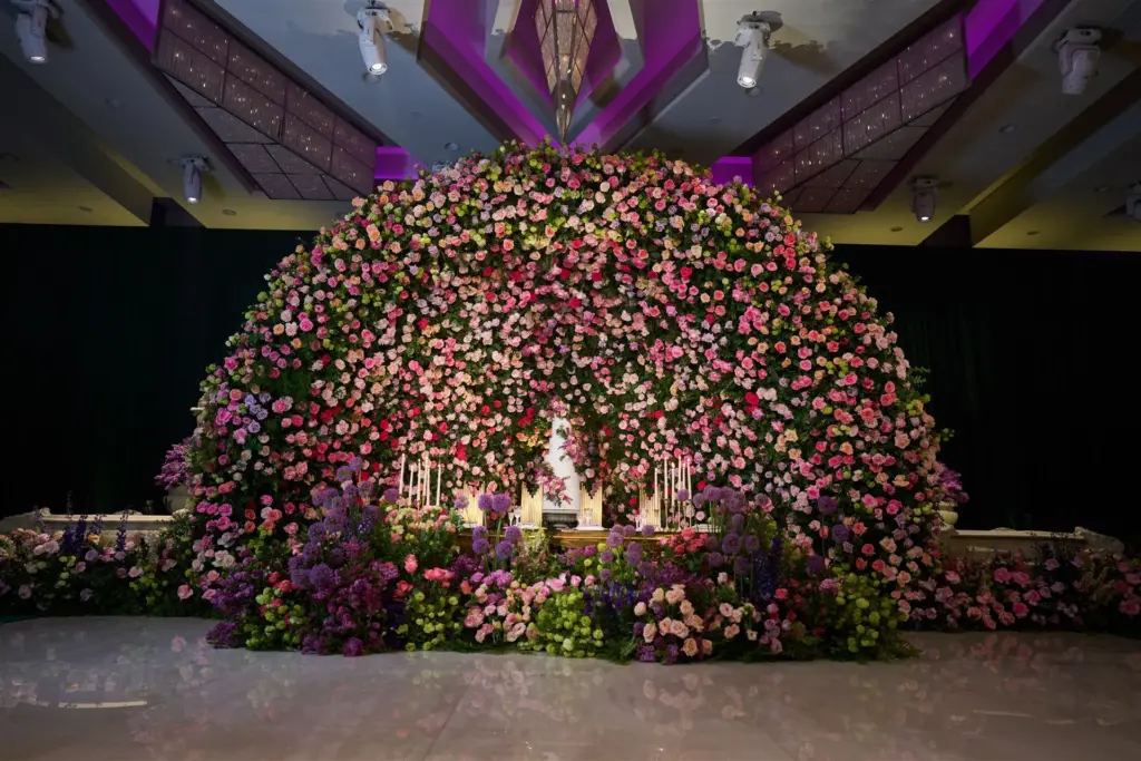 Round floral canopy surrounding a wedding cake table with purple uplighting