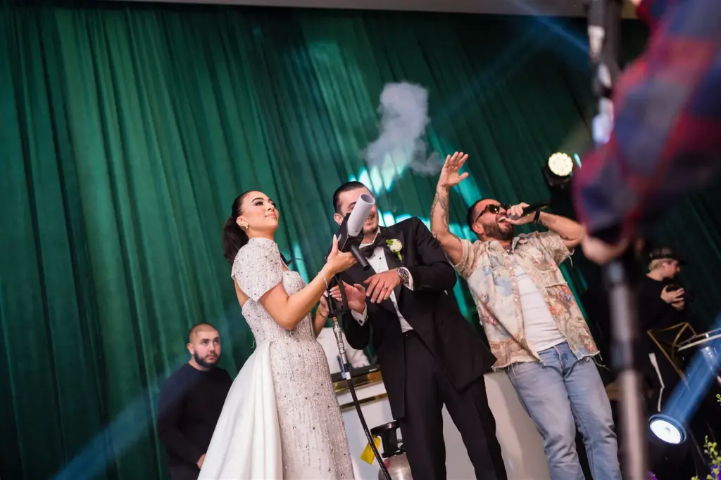 Bride and groom singing with a performer on stage during their wedding reception