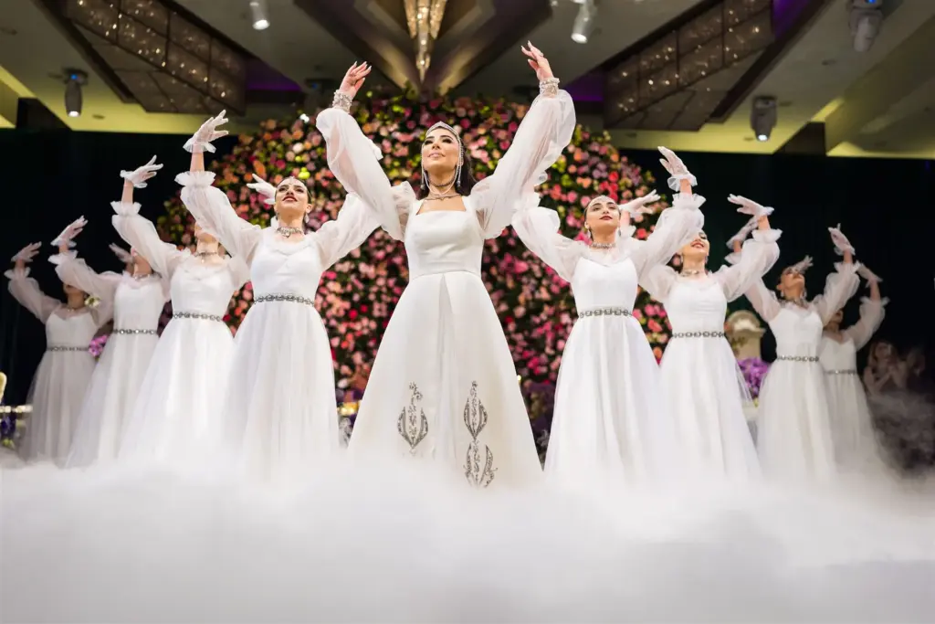 Bride and bridesmaids in white dresses dancing with raised arms amid stage fog