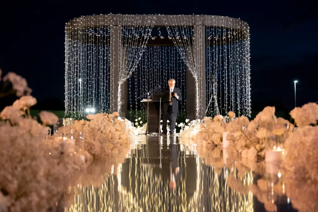 Officiant standing beneath a string-light gazebo at an outdoor wedding ceremony
