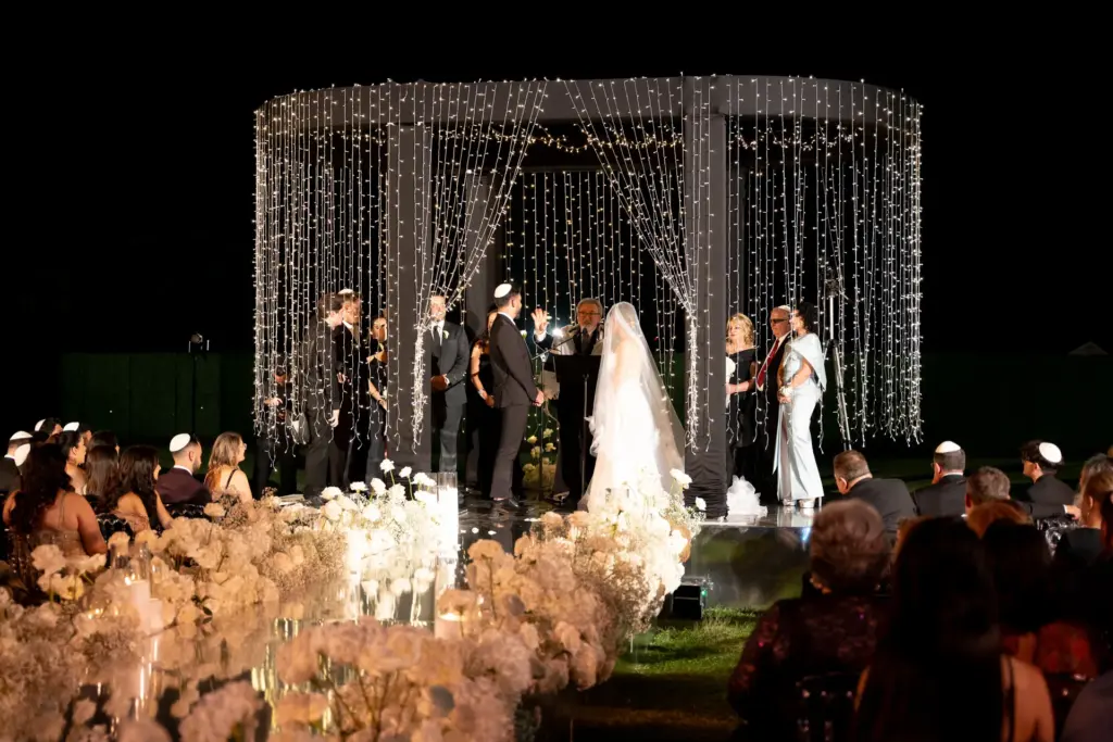 Couple exchanging vows under a lighted canopy at an outdoor evening wedding ceremony