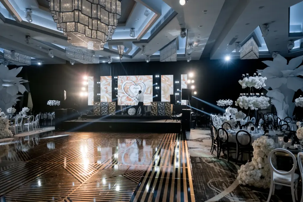 Black and gold reception ballroom with a striped dance floor and stage video screens