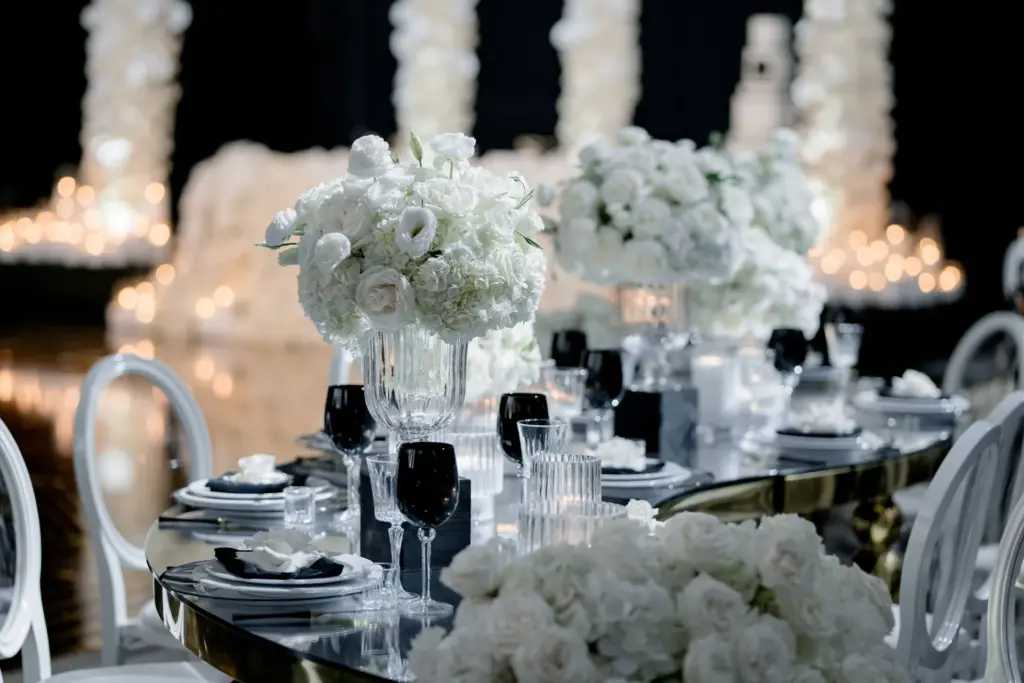 Elegant table setting with a white rose centerpiece and black wine glasses on a mirrored table