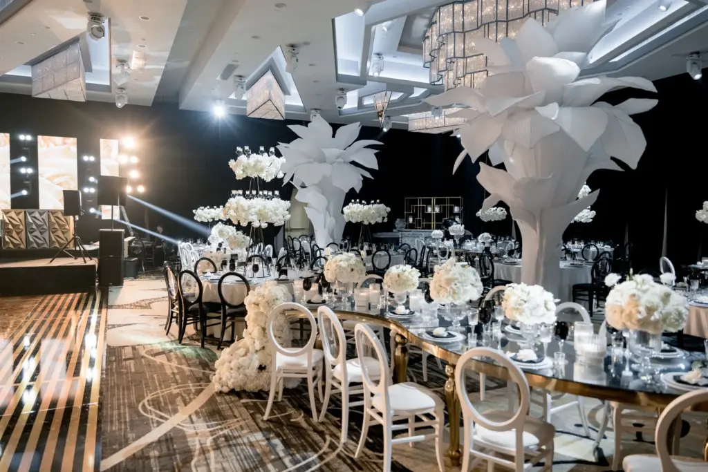 Reception ballroom with a gold-trimmed feasting table and white paper flower sculptures