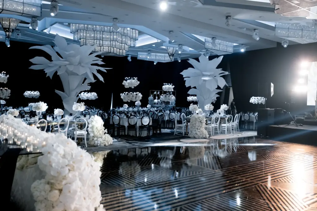 Wedding reception dance floor beneath large white paper flower sculptures and chandeliers