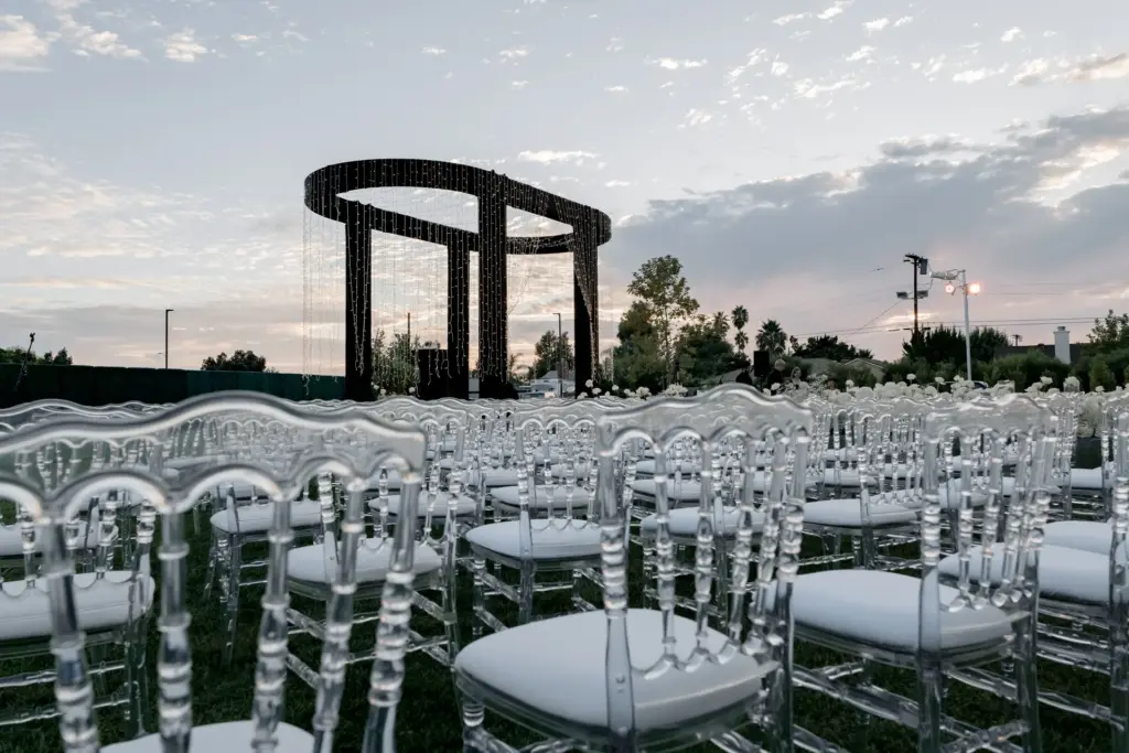 Clear chiavari ceremony chairs facing a black ring-shaped arch at dusk