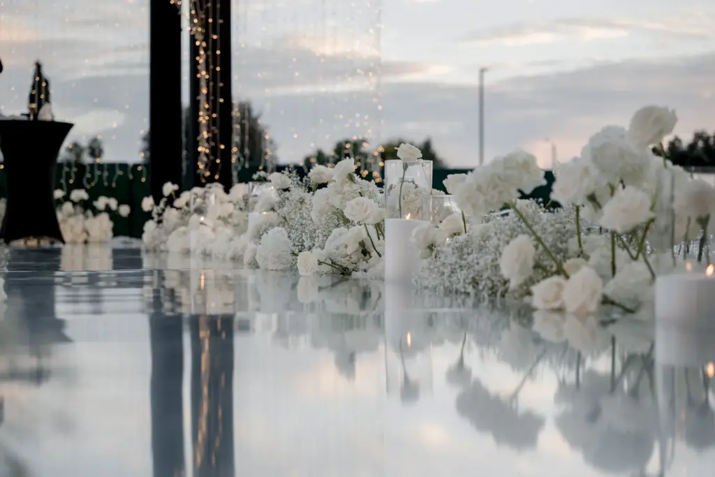 White floral aisle with candles reflecting on a glossy walkway at an outdoor evening wedding