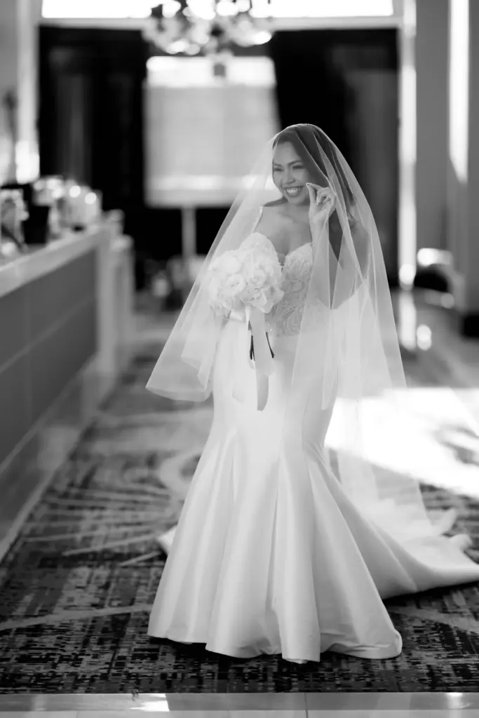Black-and-white portrait of a bride in a fitted gown and veil holding a bouquet