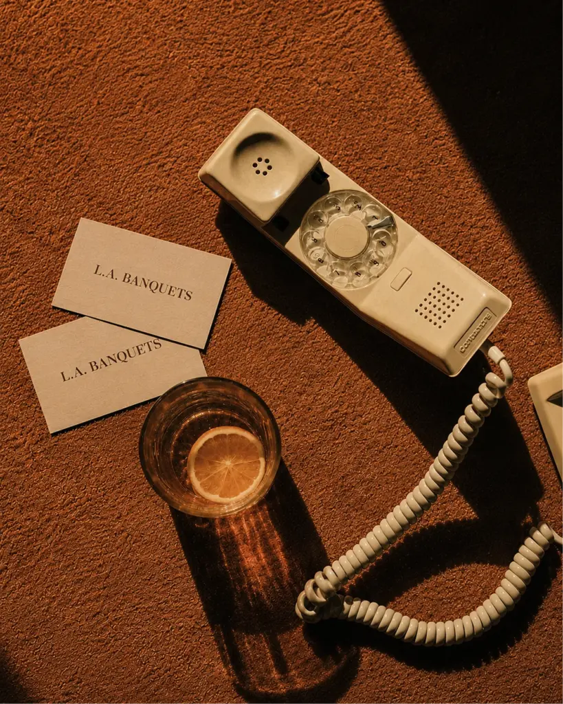 Rotary telephone, L.A. Banquets cards and a drink on a dark table